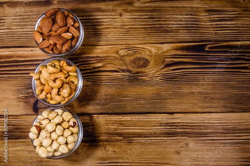 Various nuts (almond, cashew, hazelnut) in glass bowls on a wooden table. Vegetarian meal. Healthy eating concept. Top view