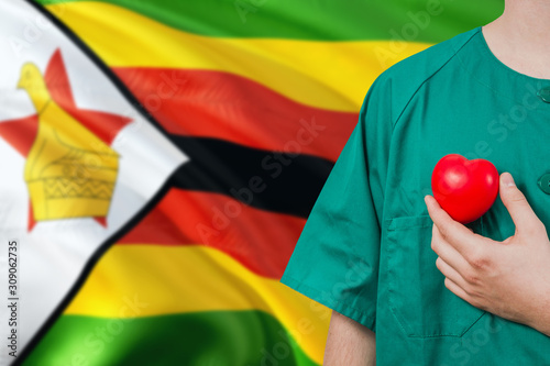 Zimbabwe veterinary clinic concept. Veterinarian is holding plastic heart in green uniform on national flag background. Animial love theme. photo