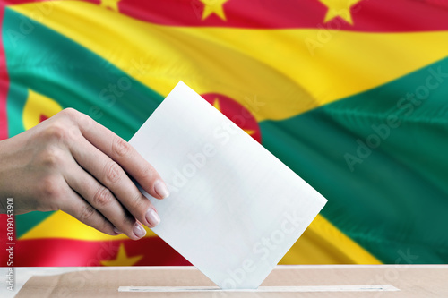 Grenada election concept. Side view woman putting a ballot in a box on national flag background.