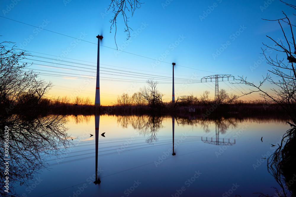 green energy, wind turbines at sunset with blue yellow heaven - reflection in water of a see green energy, wind turbines at sunset with blue yellow heaven - reflection in water of a see