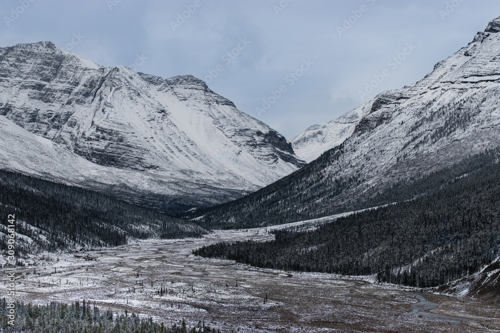 Snowy valley landscape with dry lake and high peaks covered with white snowflakes
