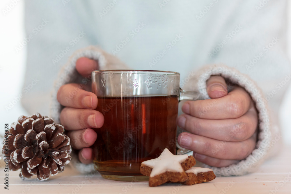 Woman holding tea with star shaped cookies and pine cone on wooden table Woman holding tea with star shaped cookies and pine cone on wooden table
