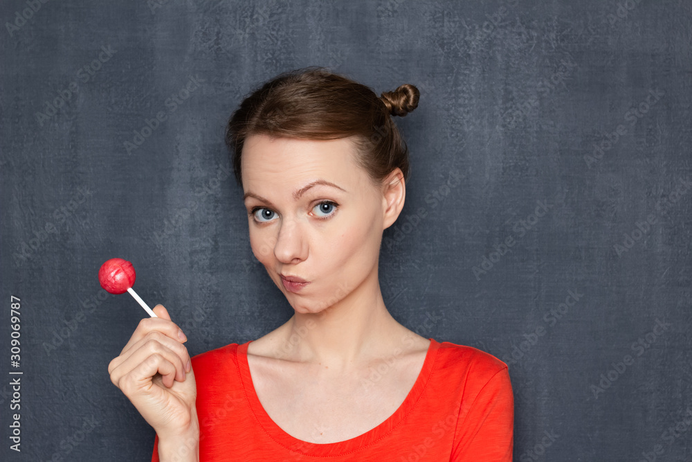 Obraz premium Portrait of thoughtful blond girl holding pink lollipop in one hand