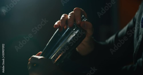 Close up of a professional bartender is preparing an alcoholic cocktail with ice cubes in a shaker to customers at the bar or disco club. photo