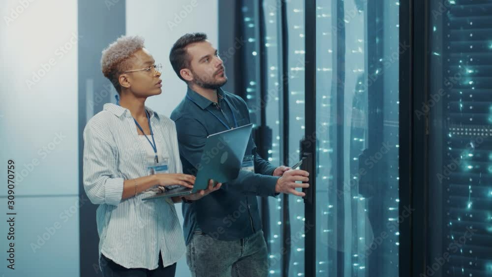 Woman chief IT admin working with male server technologist, running computer analyze on server rack cabinet, coworking in cyber security of data center. Business team.