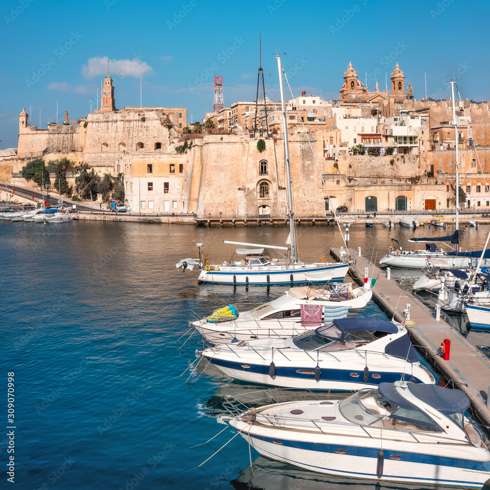Sailing boats on Senglea marina in Grand Bay, Valetta, Malta, on a bright sunny morning. Superyachts mooder by the shore. Panoramic image, swuare composition.