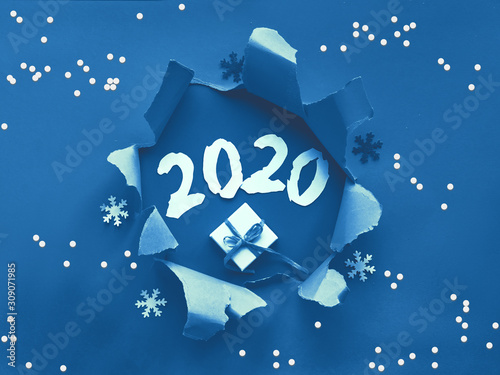 Trnedy classic blue paper flat lay with snowflakes and ripped hole in the middle. In the hole there are New Year's gift and paper number 2020. Happy New Year 2020! photo
