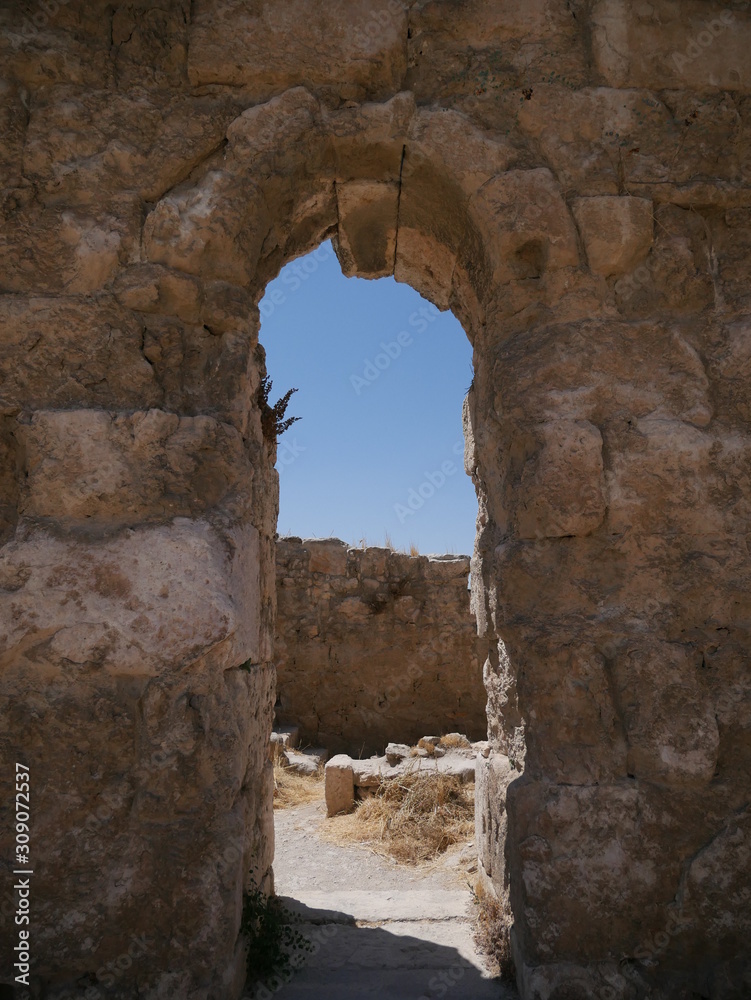 Stone wall with an arch inside of Roman ruins of the citadel of Amman, capitol of Jordan, remains of a city build from stone and tall pillars on a brown hill in the middle of a city