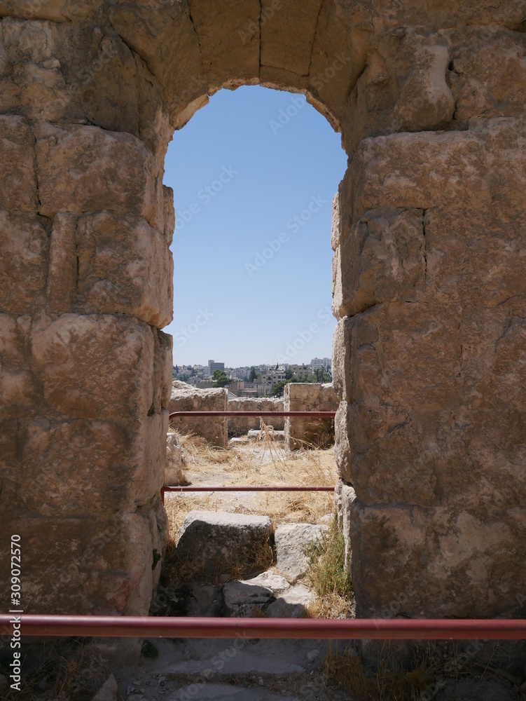 Stone wall with an arch inside of Roman ruins of the citadel of Amman, capitol of Jordan, remains of a city build from stone and tall pillars on a brown hill in the middle of a city