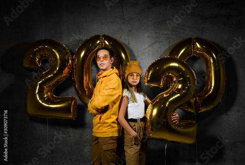 Two happy friends boy and a girl are celebrating a new year partywith ballonss numbers 2020 on a concrete background. photo