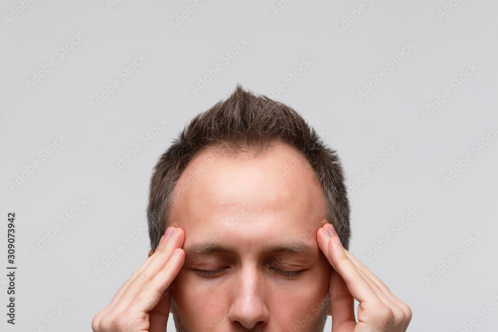 Headache, nervous tension concept. Close up portrait of man tries to concentrate, gather with thoughts, meditating and massaging his temples, closed eye, isolated on gray background. Strong migraine Headache, nervous tension concept. Close up portrait of man tries to concentrate, gather with thoughts, meditating and massaging his temples, closed eye, isolated on gray background. Strong migraine