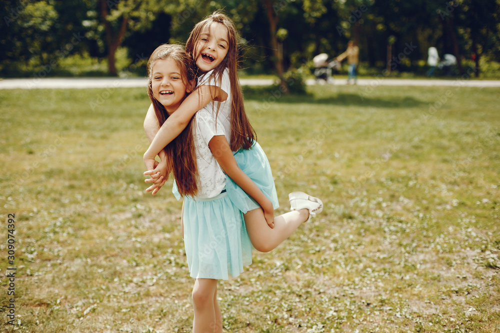Fototapeta premium two cute little girls in white T-shirts and blue skirts play in the summer park