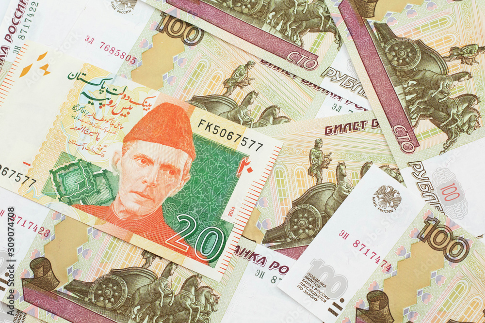 A close up image of an orange and green twenty Pakistani rupee bank note with Russian one hundred ruble bills in macro