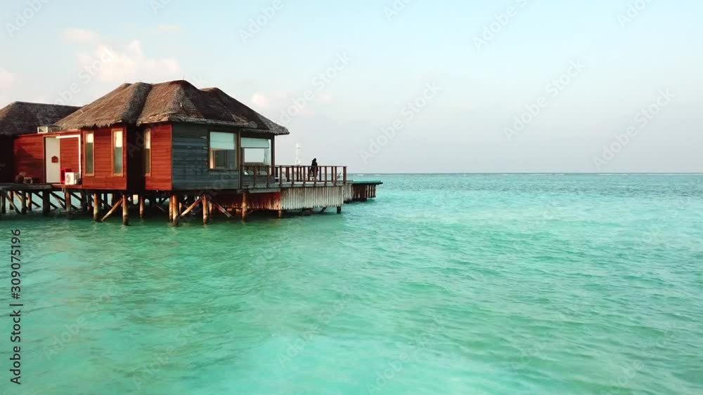 Aerial, drone shot, low over turquoise ocean, towards a girl, walking on the balcony, at a villa on the sea, on a sunny day, on the Conrad Rangali island, in Maldives Aerial, drone shot, low over turquoise ocean, towards a girl, walking on the balcony, at a villa on the sea, on a sunny day, on the Conrad Rangali island, in Maldives