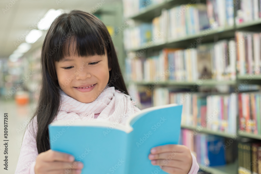 portrait of cute schoolgirl smiling while sitting with stack of books at table in library portrait of cute schoolgirl smiling while sitting with stack of books at table in library