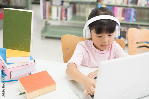 Girls are using computers to study library knowledge. She has earphones at her ear.