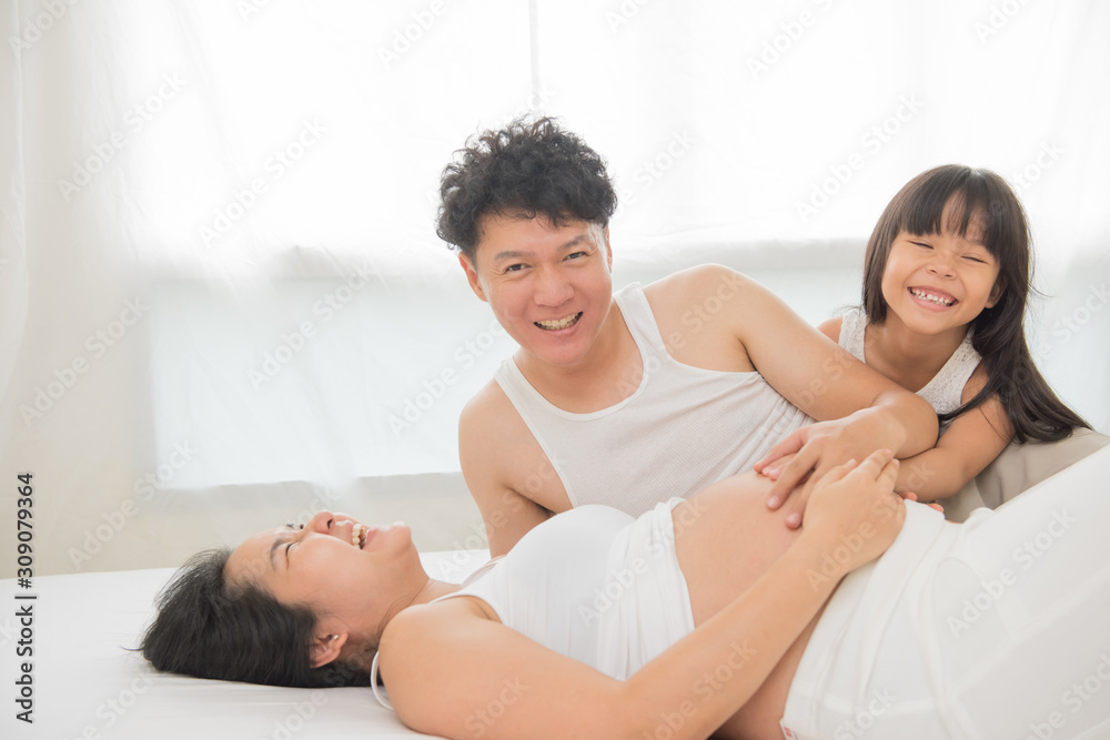 beautiful pregnant woman, her handsome husband and cute little daughter are talking and smiling in bed beautiful pregnant woman, her handsome husband and cute little daughter are talking and smiling in bed