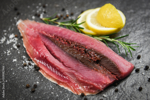Fresh fish fillet sliced for steak or salad with herbs spices rosemary and lemon - Raw fish seafood on black plate background , Longtail tuna , Eastern little tuna fillet ingredients for cooking food