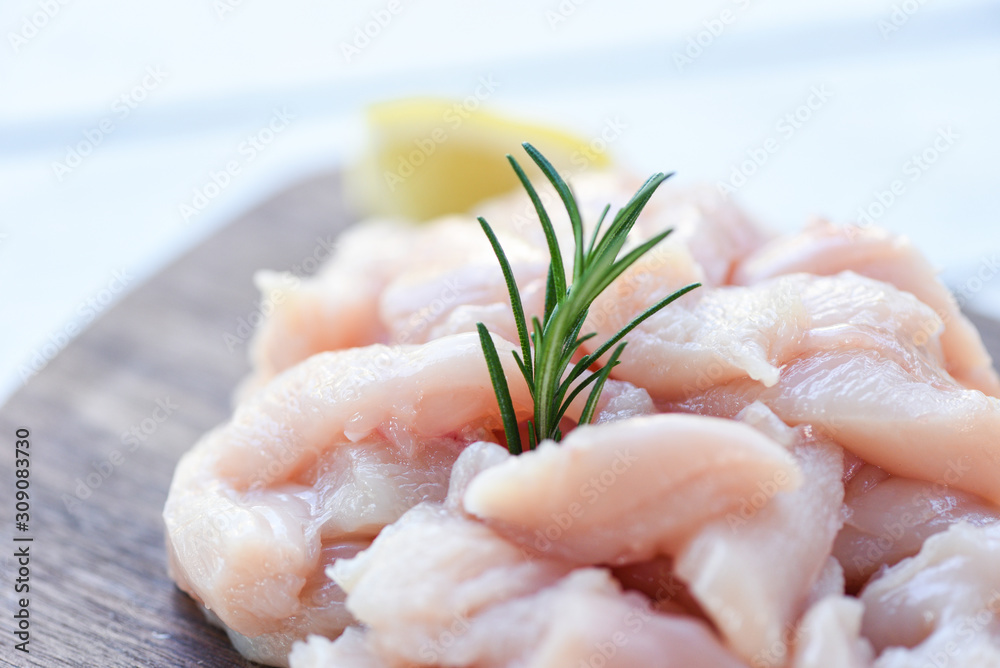 Pieces of raw chicken meat with rosemary and lemon - fresh raw cut chicken fillet on wooden cutting board background , close up Pieces of raw chicken meat with rosemary and lemon - fresh raw cut chicken fillet on wooden cutting board background , close up