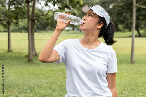 Relaxing time.Asian smiling senior woman drinking fresh water in summer at the park.