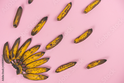  bunch of overripe spoiled mini-bananas on a pale pink background.