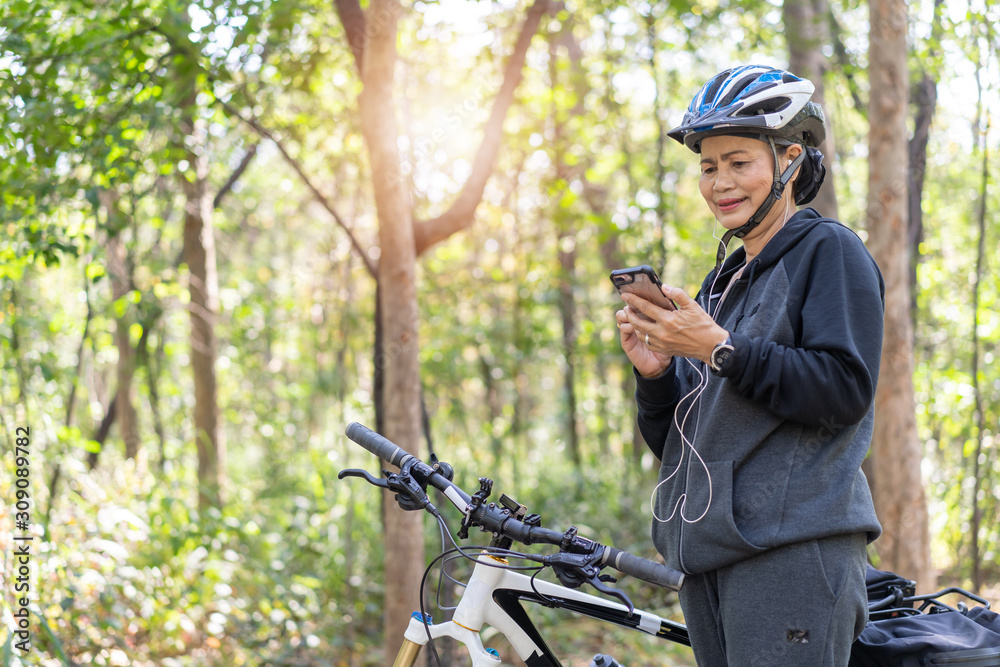 Senior asian woman bicycle in the park, With using smart phone and listening to music