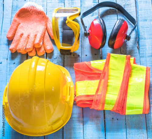 Standard construction safety equipment set including helmet, glasses, glove,  ear defenders and cloth on old blue wooden background. top view, safety first concepts
