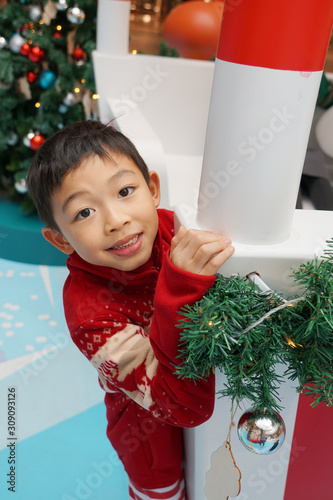 The lovely and handsome black hair  healthy Asian boy is wearing in red for Christmas theme costume during Christmas time and playing around the indoor decoration. Happy and cheerful smiling boy photo