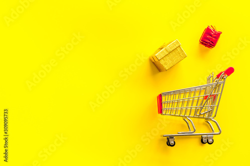 Gifts shopping. Present boxes and cart on yellow background top-down copy space