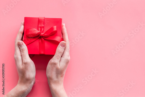 Give a gift on Valentine's Day. Women hand hold beautiful red present box on pink background top-down copy space