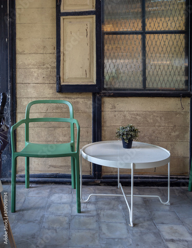 Modern green chair and white round table with green plant in vase decoration in old wooden house background.