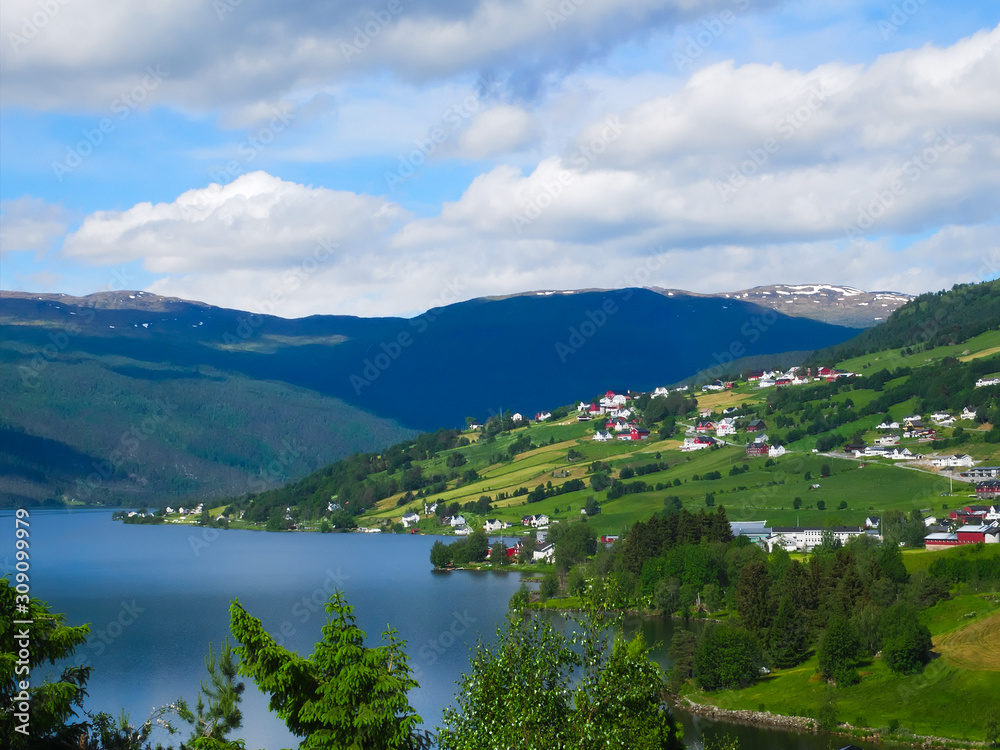 A beautiful Norwegian mountain landscape with fjord and farms in spring with blue sky and clouds.