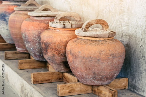 Row of earthen jars with wood lids and rough gray floor for water storage in Asian house. Selective focus on wood lids.