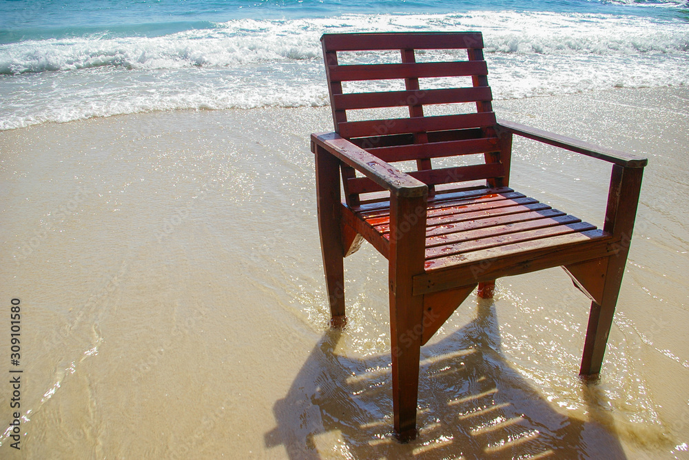 Brown wooden chairs on the beach were swept by the waves on a bright blue day. Brown wooden chairs on the beach were swept by the waves on a bright blue day.
