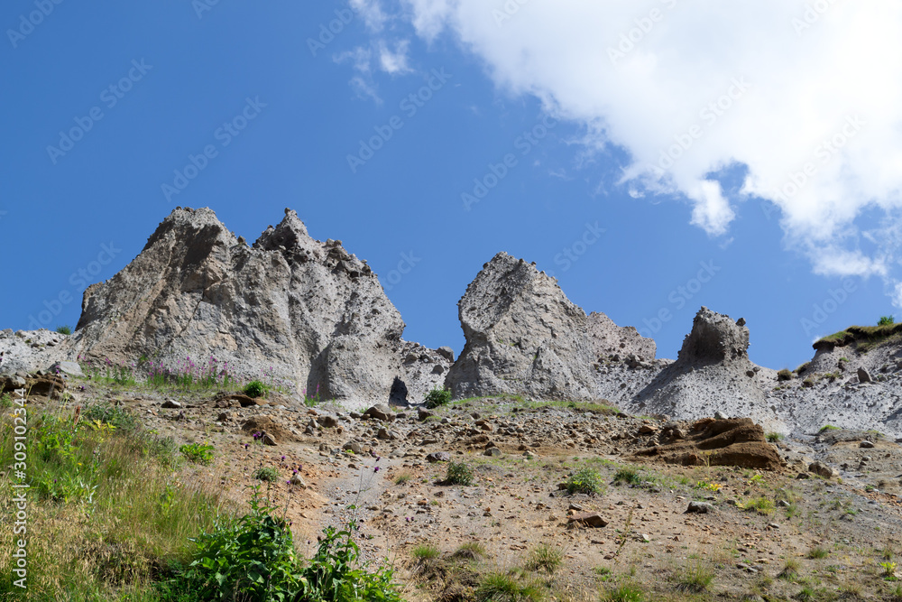 Nature background. Rocks against a bright blue sky and a fluffy white cloud