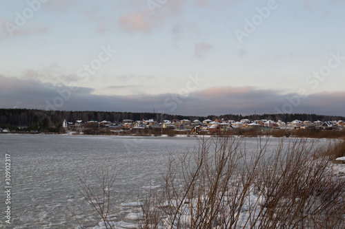 Winter landscape. View of the frozen lake, village and cloudy sky 