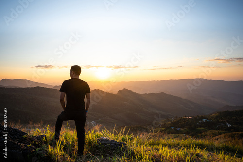 Silhouette lonely man standing and relaxing on the rock in front of the beautiful mountain background in sunset.Chilling out freedom on a good time.Summer vacation, happy holidays, travel concept.