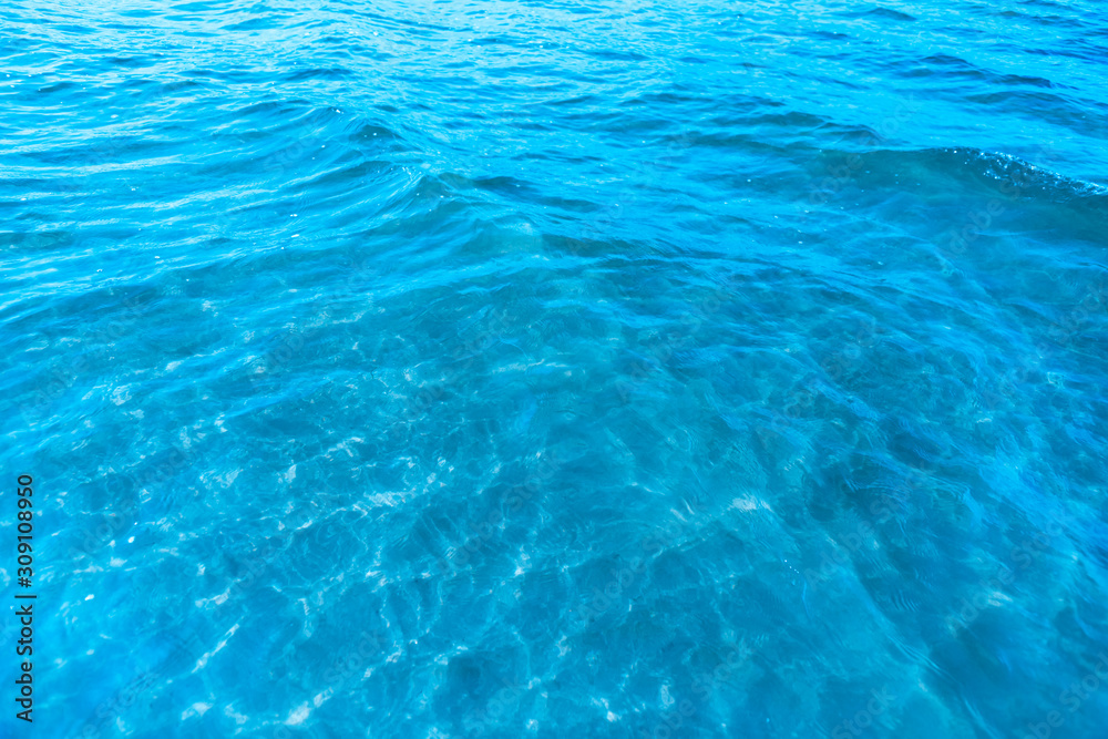 Obraz premium Blue transparent sea water near the beach texture background. clear water surface with slight waves and glare on a sunny day. sea ​​vacation