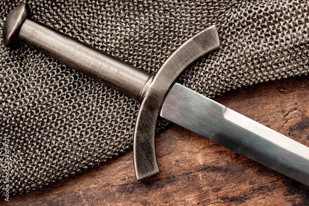 Medieval weapons and middle ages warfare conceptual idea with close up on sword on steel chain mail or maille on wooden background