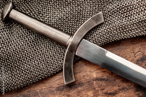 Obraz na płótnie Medieval weapons and middle ages warfare conceptual idea with close up on sword on steel chain mail or maille on wooden background w salonie