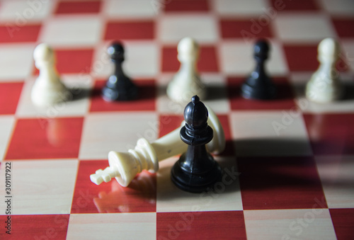 Symbolic shot on chess board. White king is taken down by black bishop and army of white and black pawns in standing behind