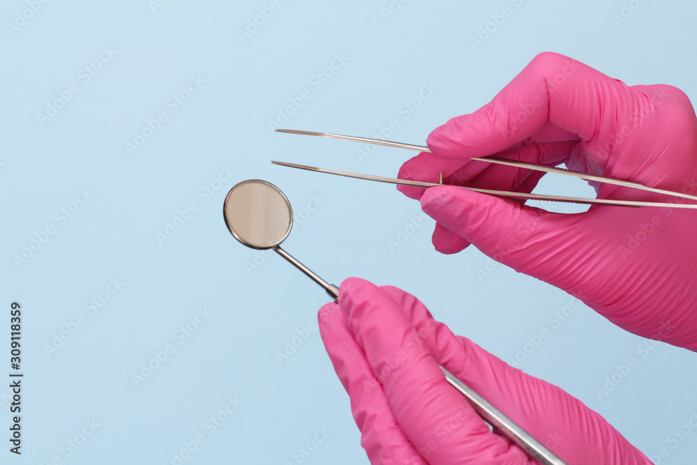 Dentist's hands with tweezers and mouth mirror.