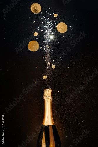 Champagne bottle with gold splashes, glitters and golden decoration on black background. Flat lay. Minimal Christmas winter party concept