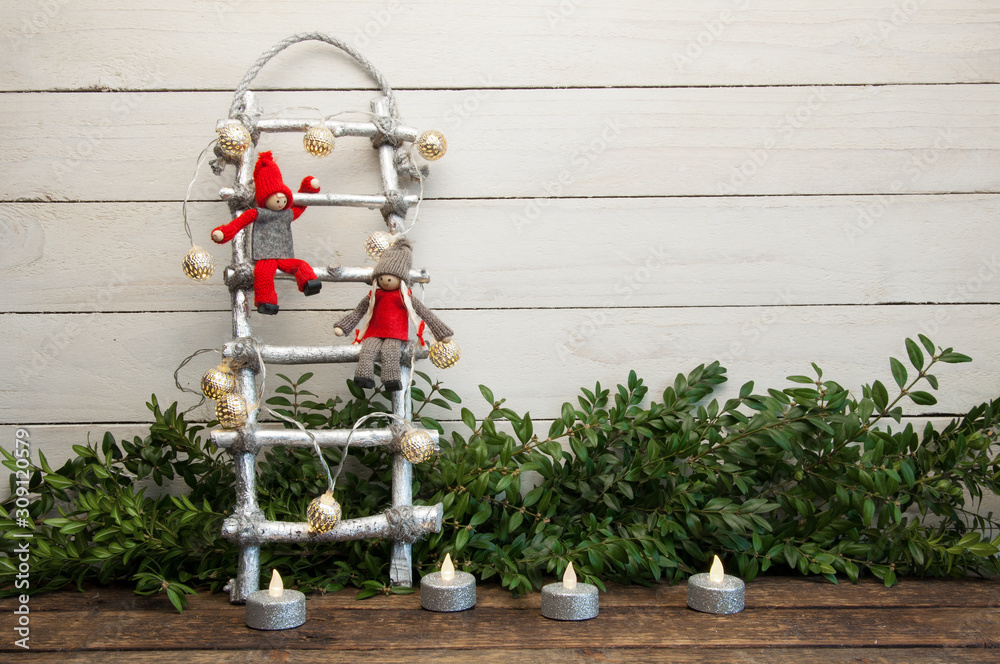 Little dwarf dolls are sitting on the Christmas stairs. White wood background