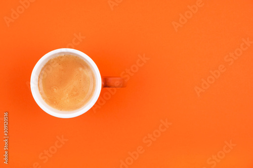 Fresh brewed coffee in ceramic cup over orange background. Place for text.
