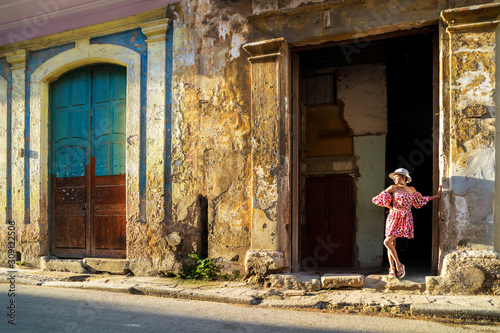 Young woman in a colored dress stands at the wall of a house on the street in the sunshine 