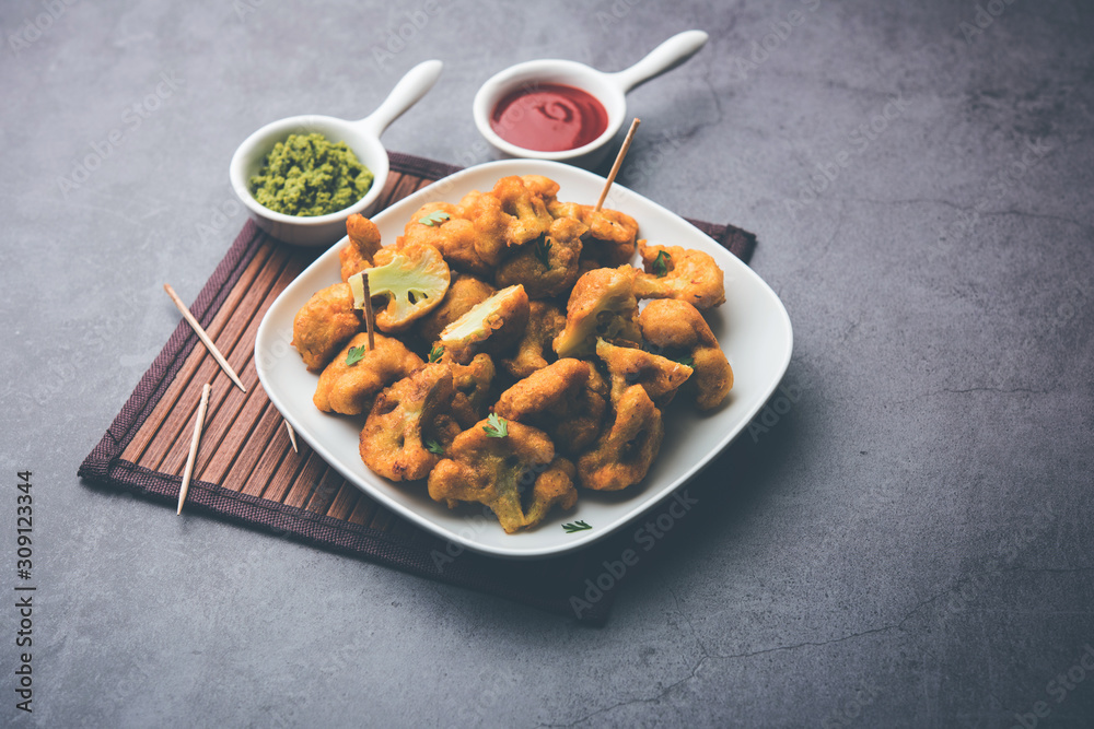 Gobi pakora or Phoolgobi pakoda made using fresh cauliflower dipped chickpea batter and then fried in oil. served with tomato ketchup and mint chutney. selective focus Gobi pakora or Phoolgobi pakoda made using fresh cauliflower dipped chickpea batter and then fried in oil. served with tomato ketchup and mint chutney. selective focus