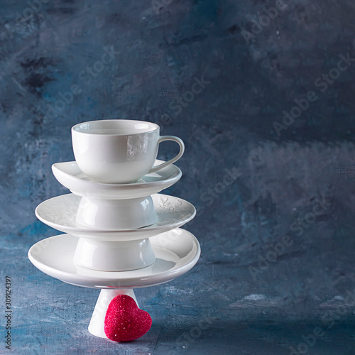 White saucer pyramid with cup on top and one red heart candy on it Dark background. Creative concept, love, relations, gift, celebrate, restaurant, food, St. Valentine's day. Square copy space photo