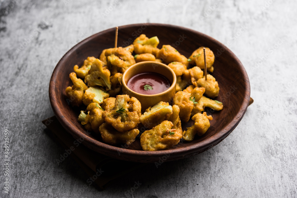 Gobi pakora or Phoolgobi pakoda made using fresh cauliflower dipped chickpea batter and then fried in oil. served with tomato ketchup and mint chutney. selective focus