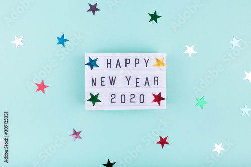 Light board with text HAPPY NEW YEAR 2020 on mint color background with stars. Flat lay, copy space, top view. Festive decorations 2020 celebration. New Year. Merry Christmas card. 